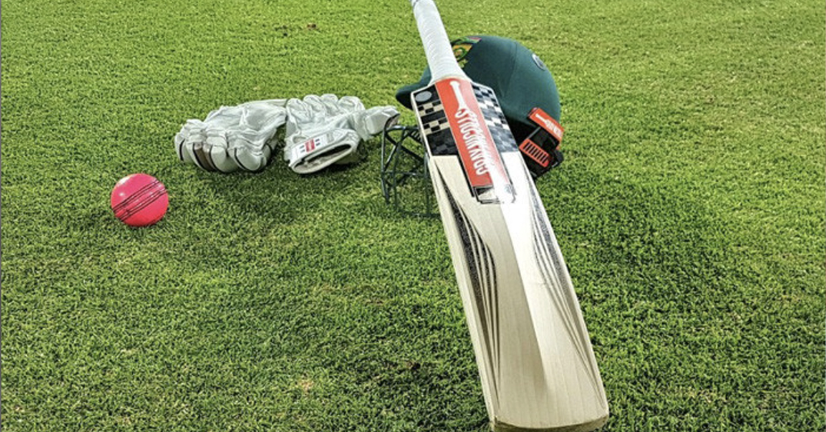 Cricket bat, helmet, golves, and ball lying on grass