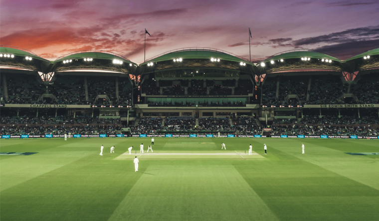 Floodlit cricket stadium with match in progress